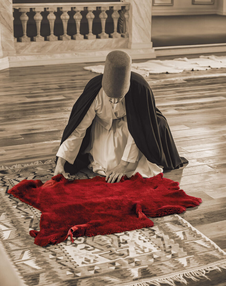 A Mevlevi sheikh in a black cloak kneeling on the red sheepskin post, the seat of the sheikh during the Sema