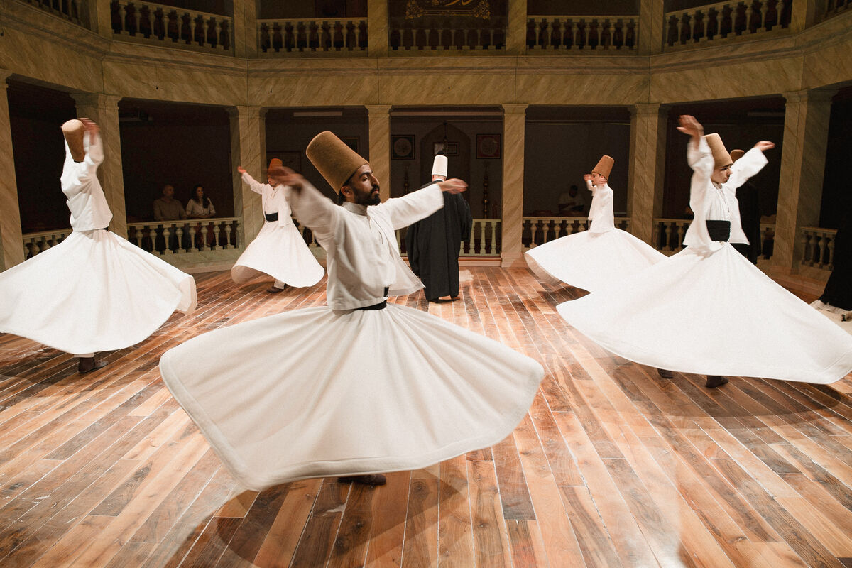 Whirling dervishes in white tennure skirts and camel felt hats turning on the wooden floor of the Kasımpaşa Mevlevihanesi ceremony hall