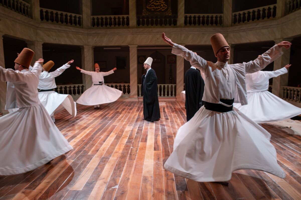 Several whirling dervishes in white tennure skirts and camel felt hats turning in the hall at Kasımpaşa Mevlevihanesi